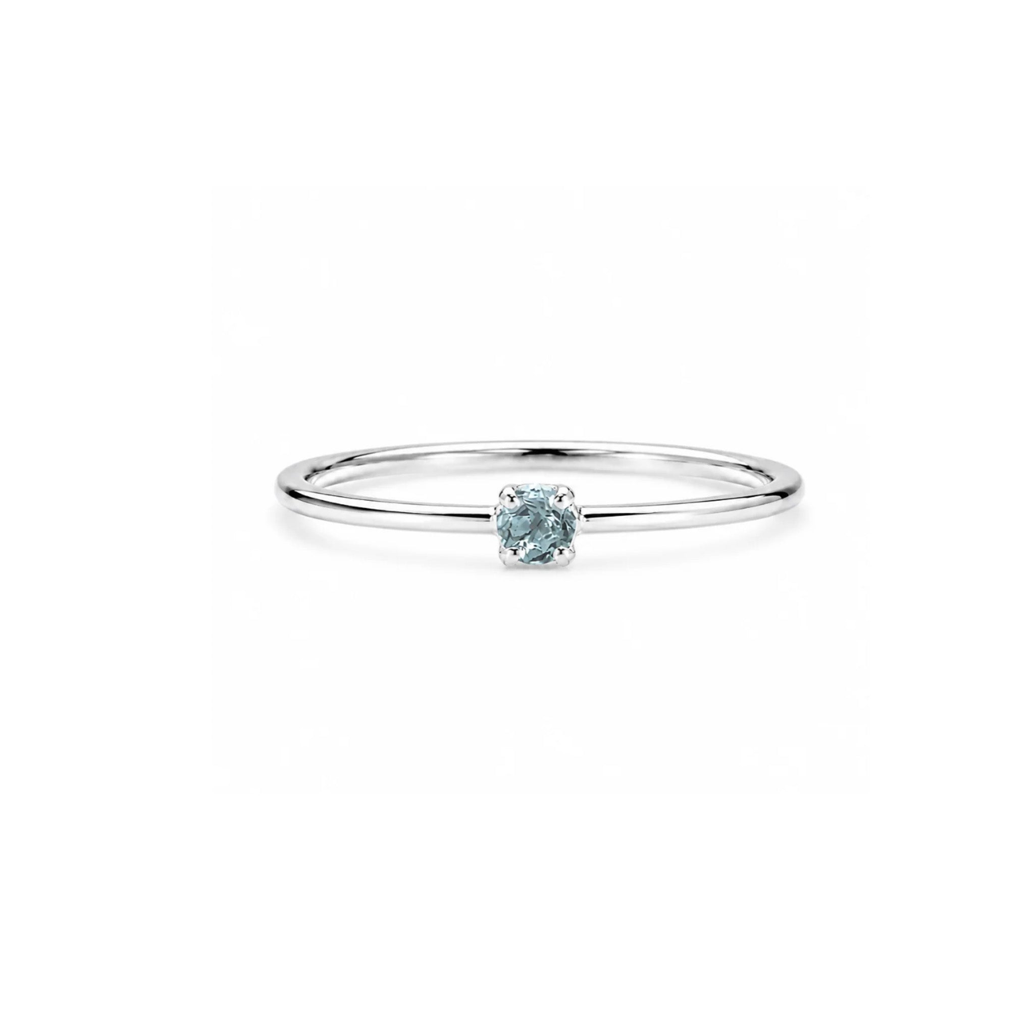 A delicate sterling silver ring featuring a single round-cut light blue gemstone in a prong setting