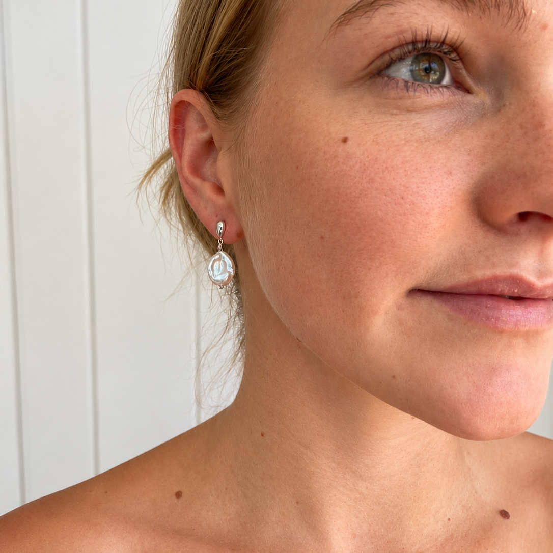 Close-up of model wearing Coastal Dew Drop 12mm white baroque freshwater pearl drop earrings in sterling silver, designed in Broome by Lush Designs Jewellery.
