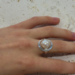 Hand wearing a ring with a pearl on a textured surface