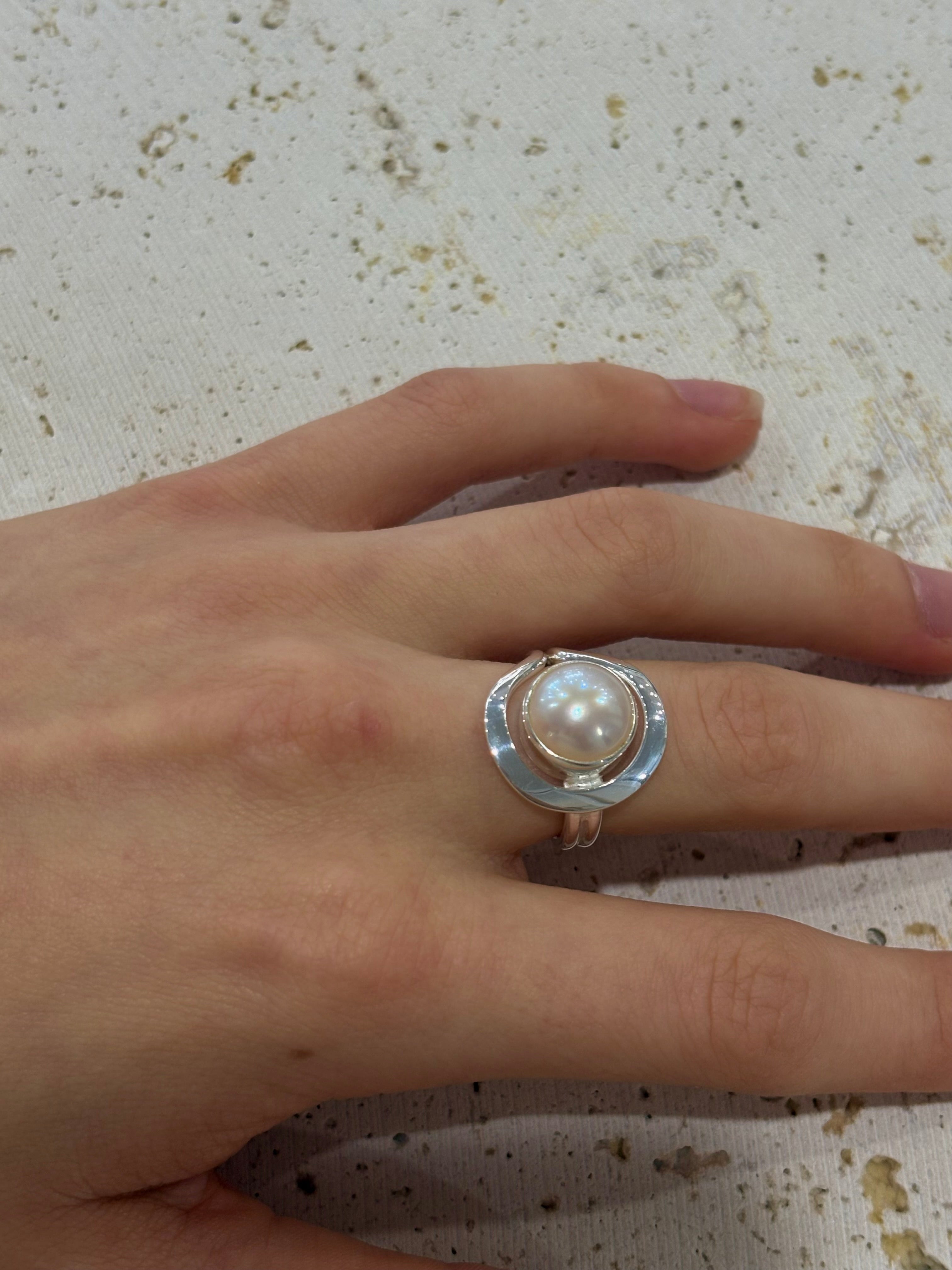 Hand wearing a ring with a pearl on a textured surface