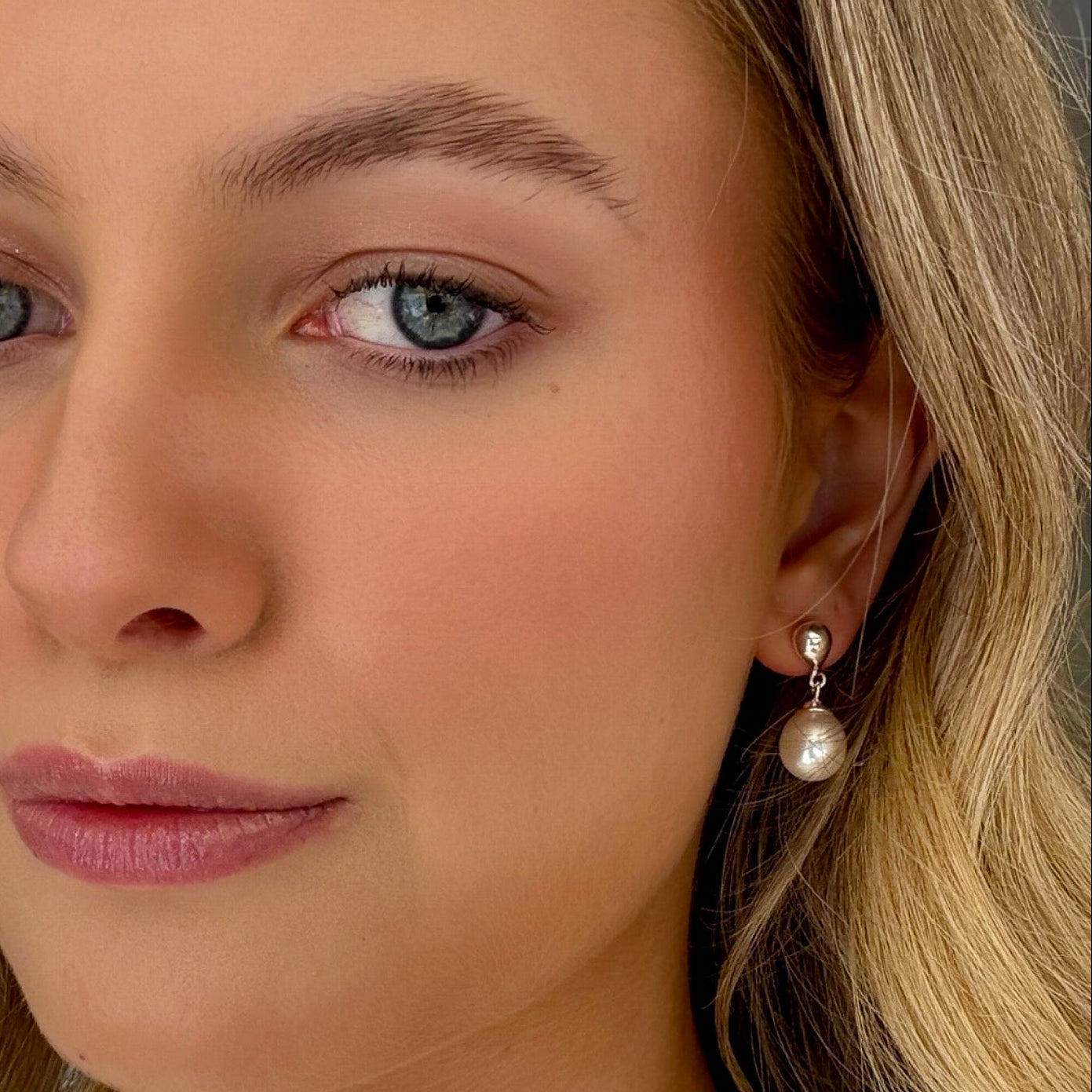 Close-up of a woman with blonde hair and blue eyes wearing pearl earrings.