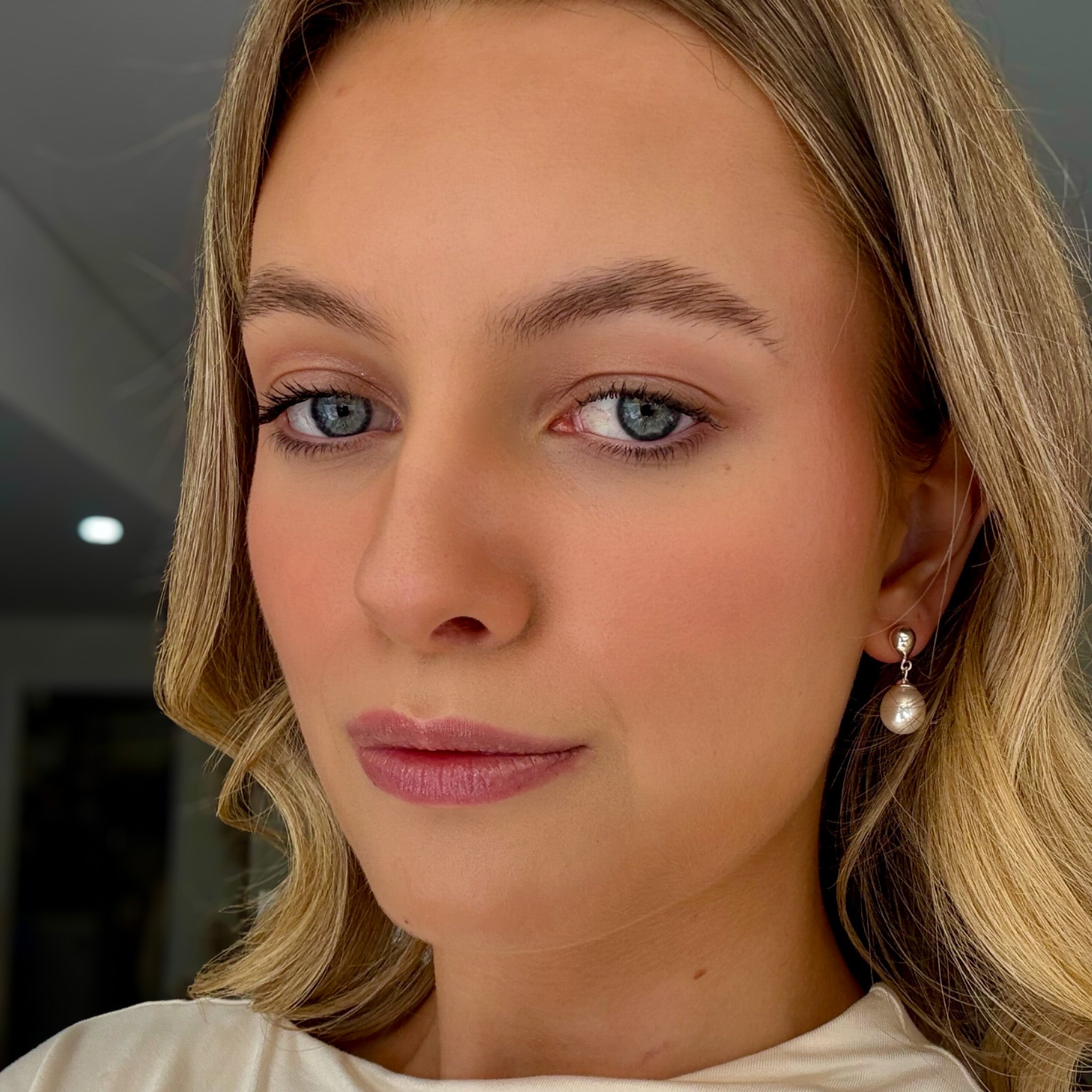 Close-up of a woman with blonde hair and blue eyes wearing pearl earrings.