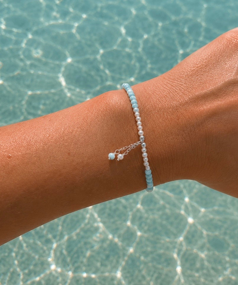 Light blue gemstone and freshwater pearl bracelet featuring delicate white pearls, soft blue beads and sterling silver accents on an adjustable design. A beach-inspired bracelet handcrafted for effortless coastal style.
