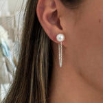 A close-up image of a woman's ear wearing a silver earring with a white pearl drop.