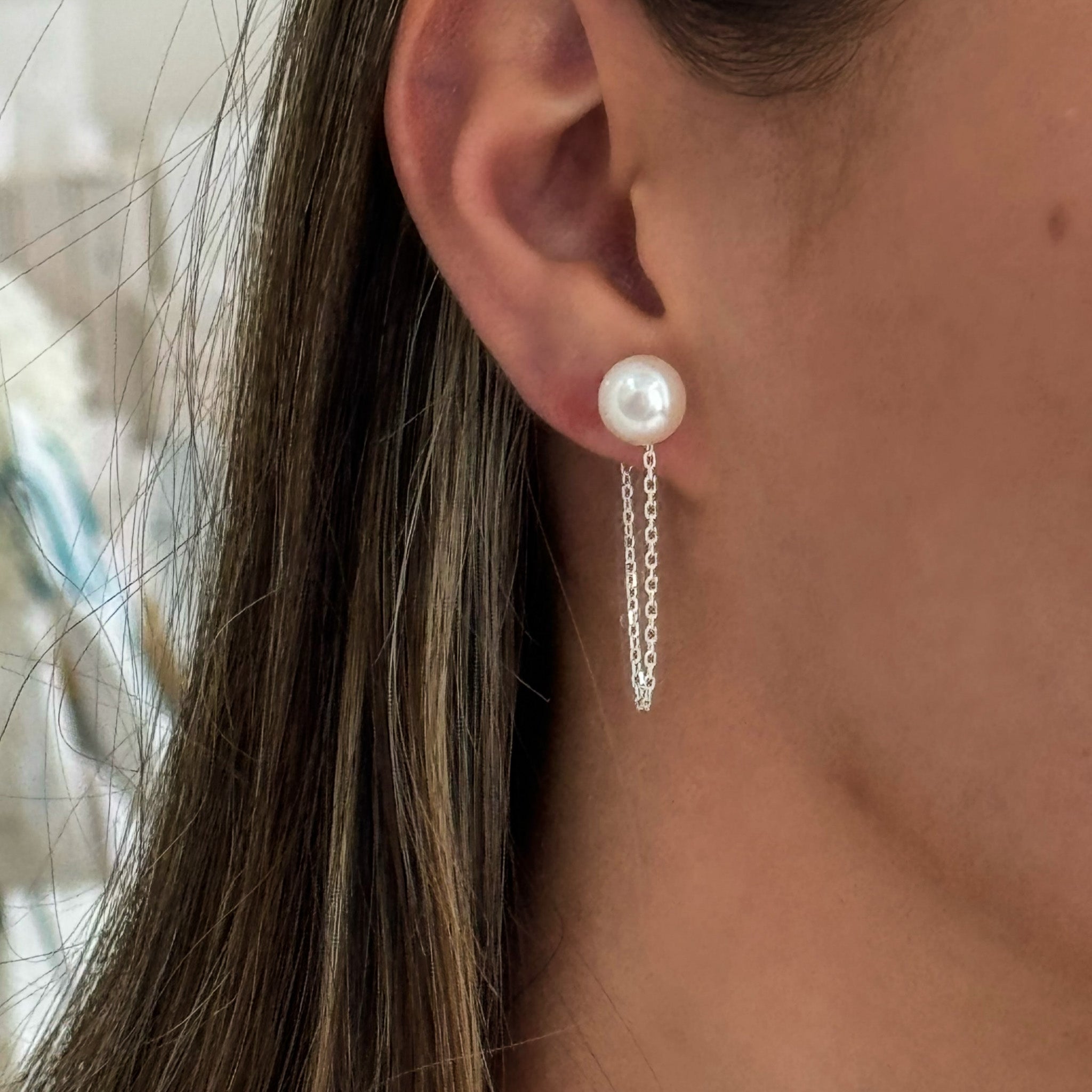 A close-up image of a woman's ear wearing a silver earring with a white pearl drop.