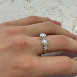 Hand wearing a silver ring with three pearls on a textured surface
