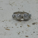 Silver ring with three circular stones on a textured white background