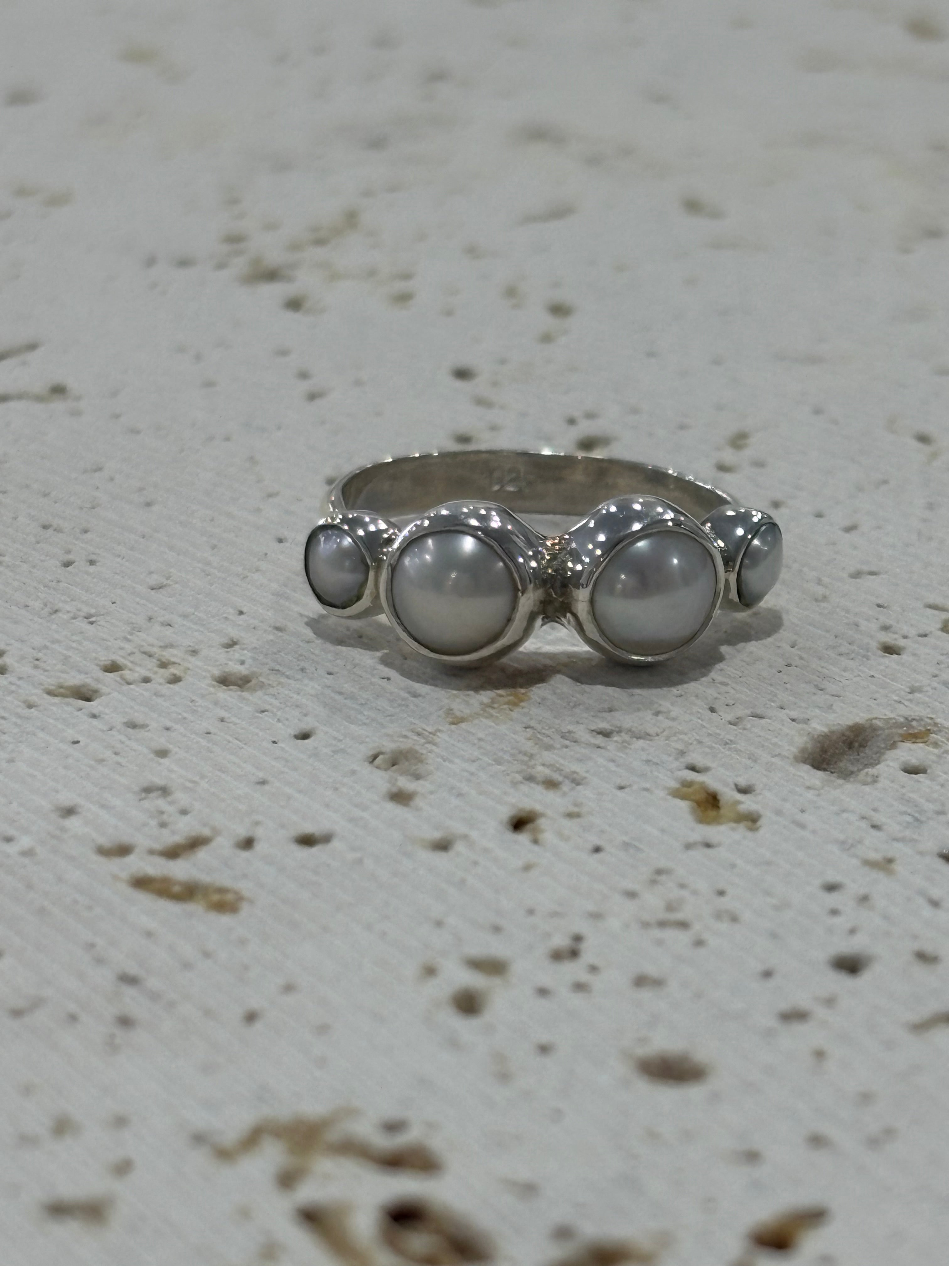 Silver ring with three circular stones on a textured white background