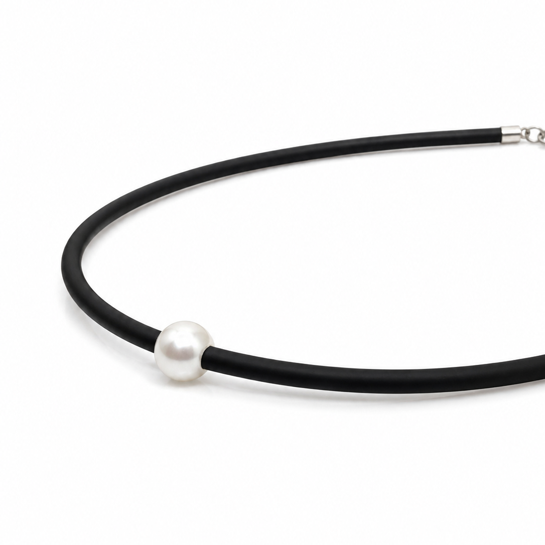 A minimalist black neoprene necklace featuring a single white pearl bead and a silver lobster clasp.
