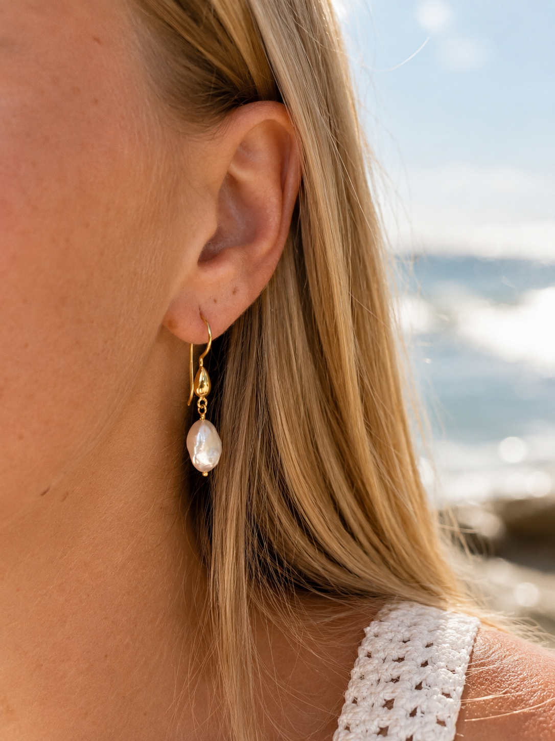 Coastal Dew Drop 12mm baroque pearl hook earrings in gold vermeil worn by the beach – Lush Designs Jewellery Australia