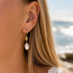 Coastal Dew Drop 12mm baroque pearl hook earrings in gold vermeil worn by the beach – Lush Designs Jewellery Australia