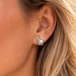 A close-up of a woman's ear wearing a silver turtle stud earring with a white pearl in the center.