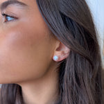 Close-up of a woman's ear wearing a small earring with a blurred background