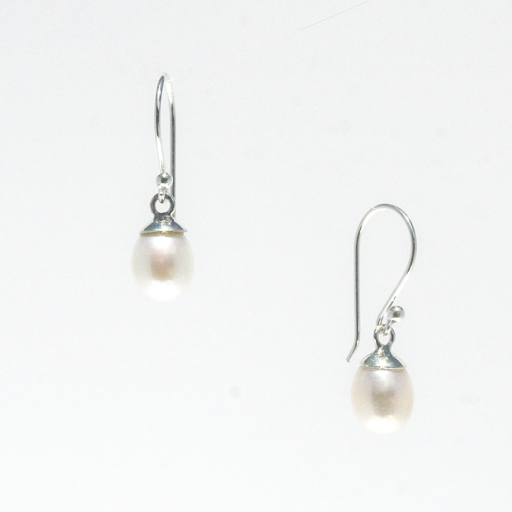 A pair of dainty silver hook earrings with white freshwater pearls attached, displayed against a white background.