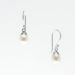 A pair of dainty silver hook earrings with white freshwater pearls attached, displayed against a white background.